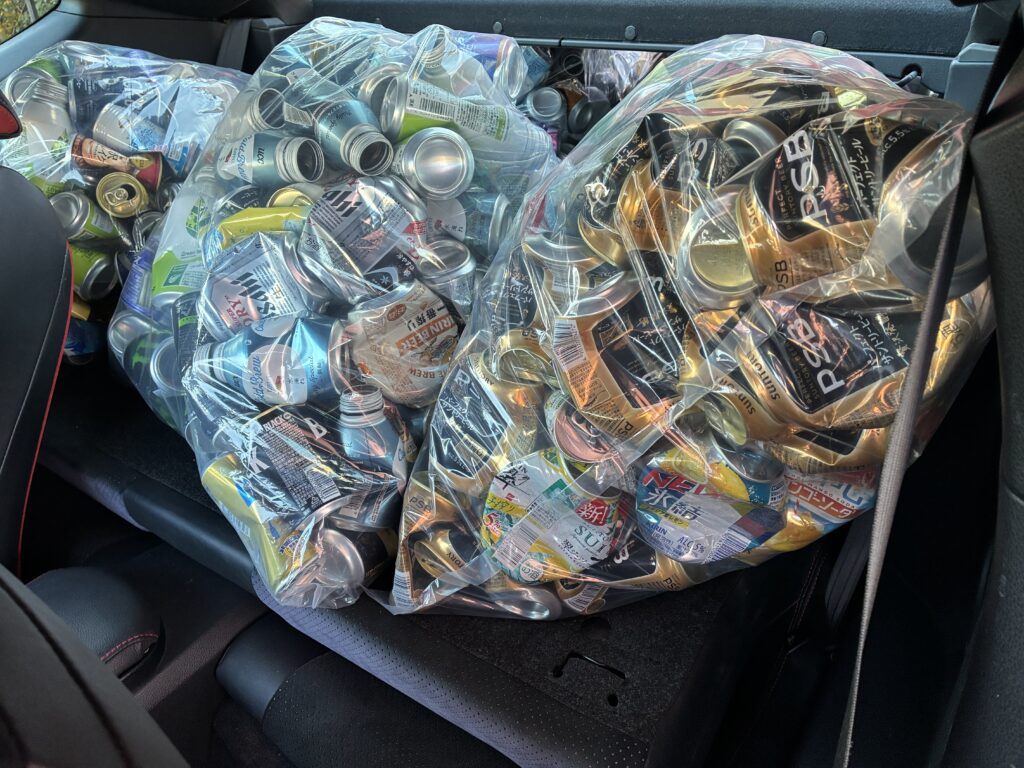 車の後部座席に45Lポリ袋に入ったアルミ缶を3袋積み込んだ様子。袋が座席いっぱいに広がり、輸送の限界容量に近い状態がわかる写真。